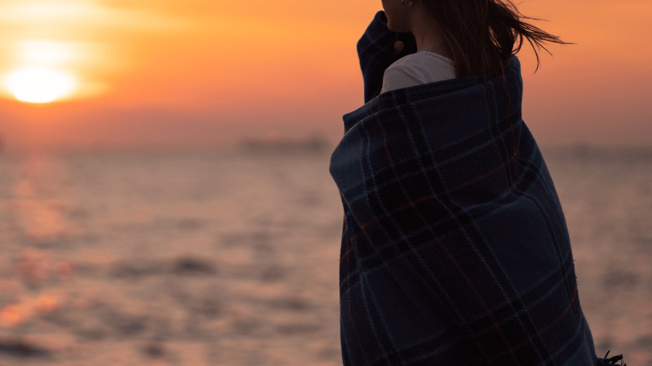 Mujer mirando el mar al atardecer envuelta en una manta