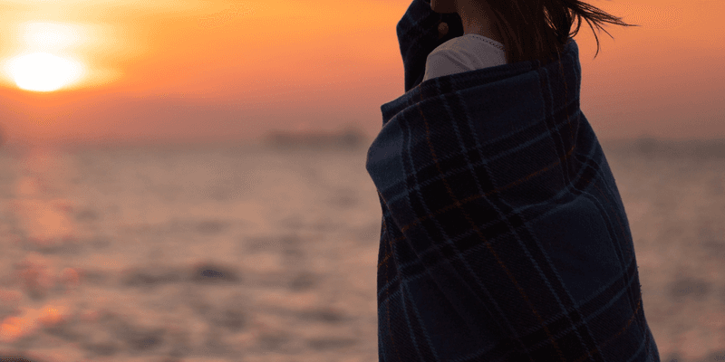 Mujer mirando el mar al atardecer envuelta en una manta