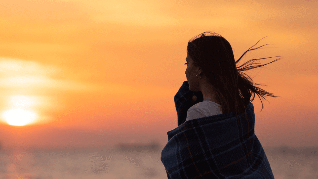 Mujer mirando el mar al atardecer envuelta en una manta