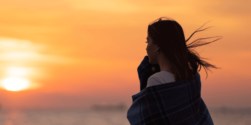 Mujer mirando el mar al atardecer envuelta en una manta