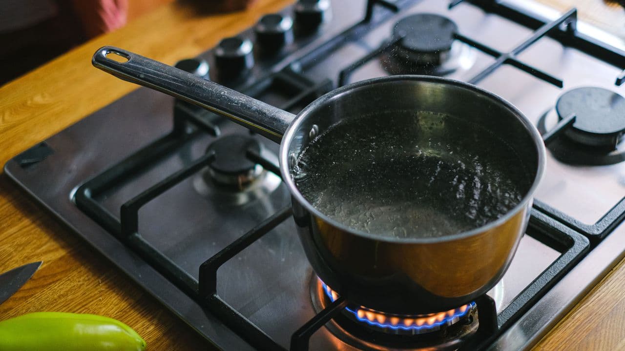 Persona hirviendo agua en un cazo en la cocina