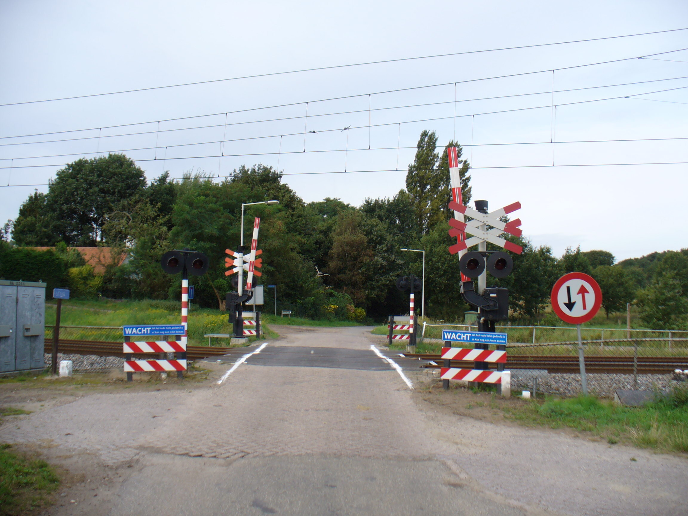 Un cruce ferroviario rural en los Países Bajos con señales de advertencia y barreras de seguridad recién instaladas para prevenir accidentes.