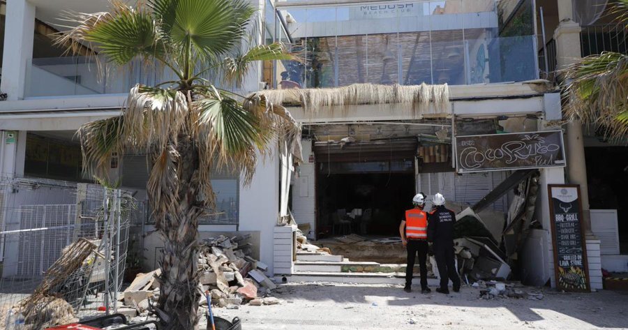 Restaurante derrumbado en Mallorca, con equipos de rescate trabajando en el lugar, y turistas observando el incidente.